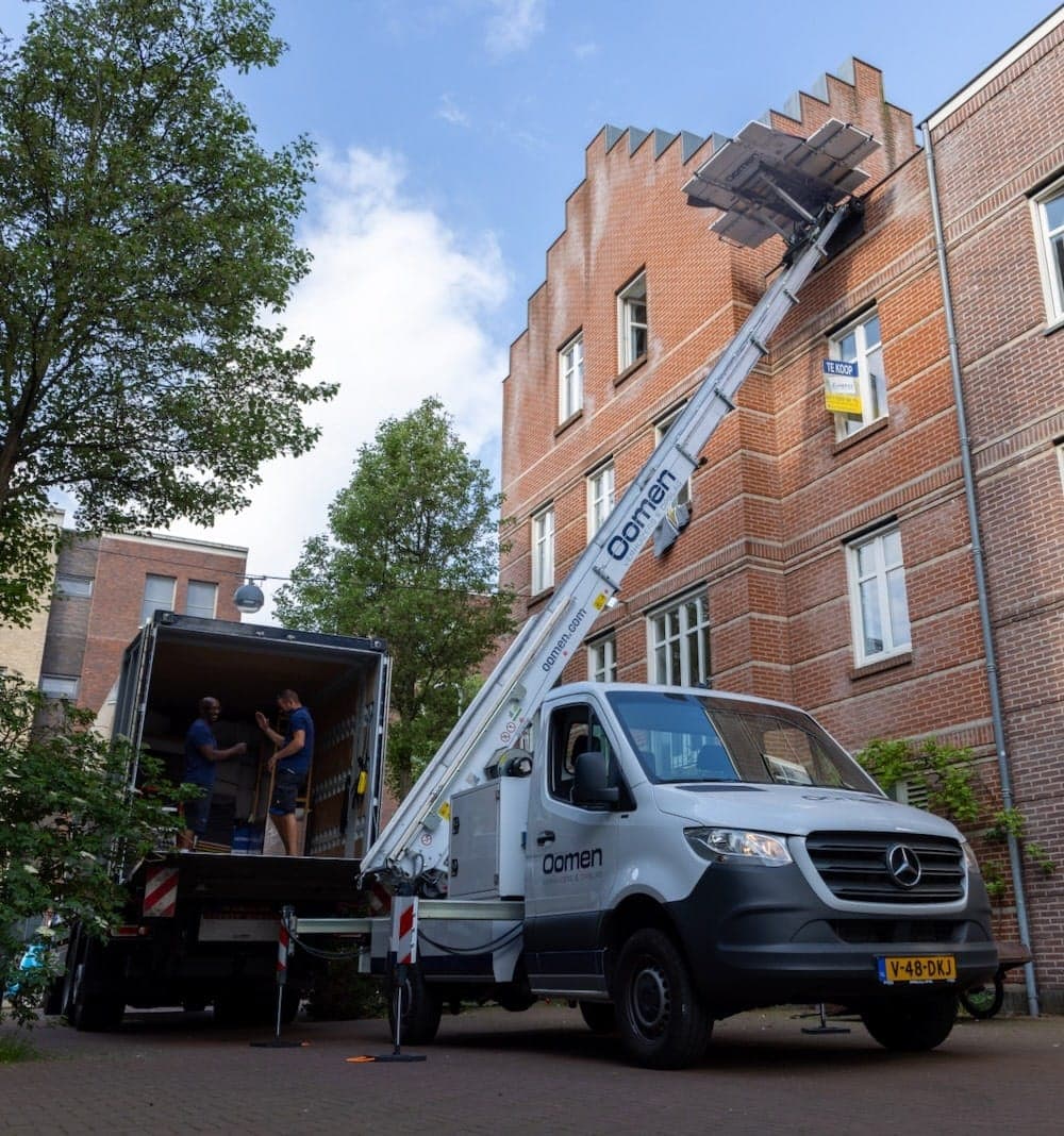 Verhuislift van Oomen tegen een bakstenen appartementengebouw, terwijl verhuizers de verhuiswagen laden