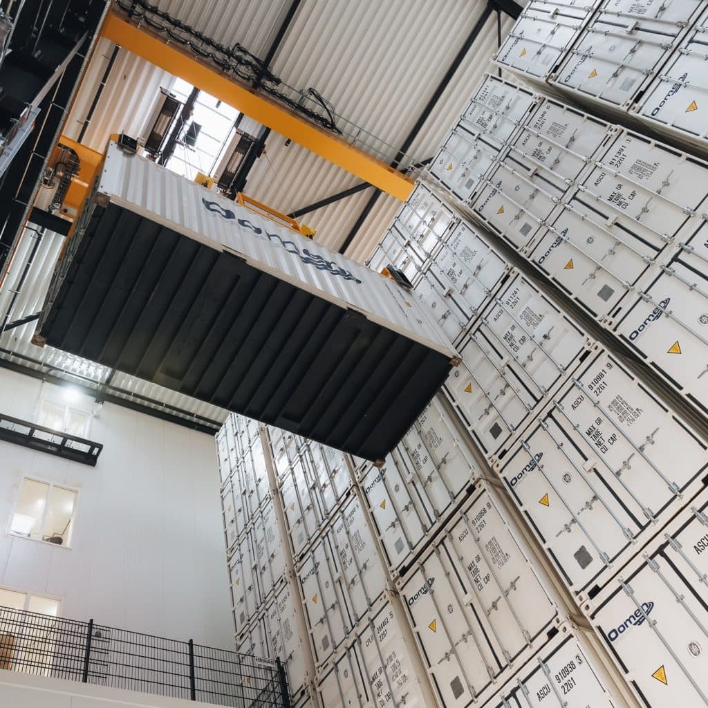 Opslagcontainer van Oomen wordt met een bovenloopkraan in de opslaghal getild